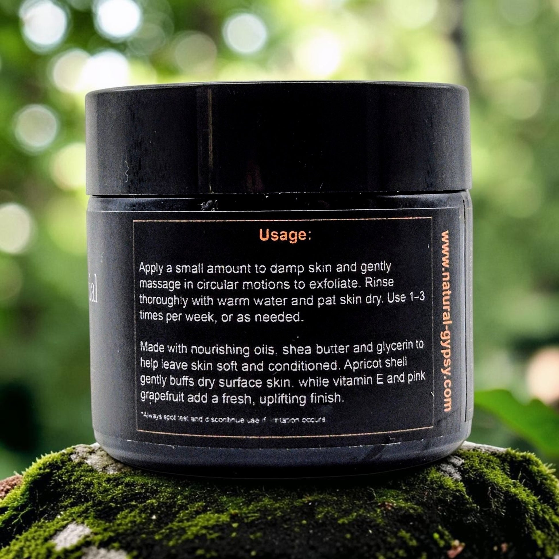Natural Gypsy Apricot Glow Facial Scrub black jar with usage instructions on a mossy surface in a forest setting