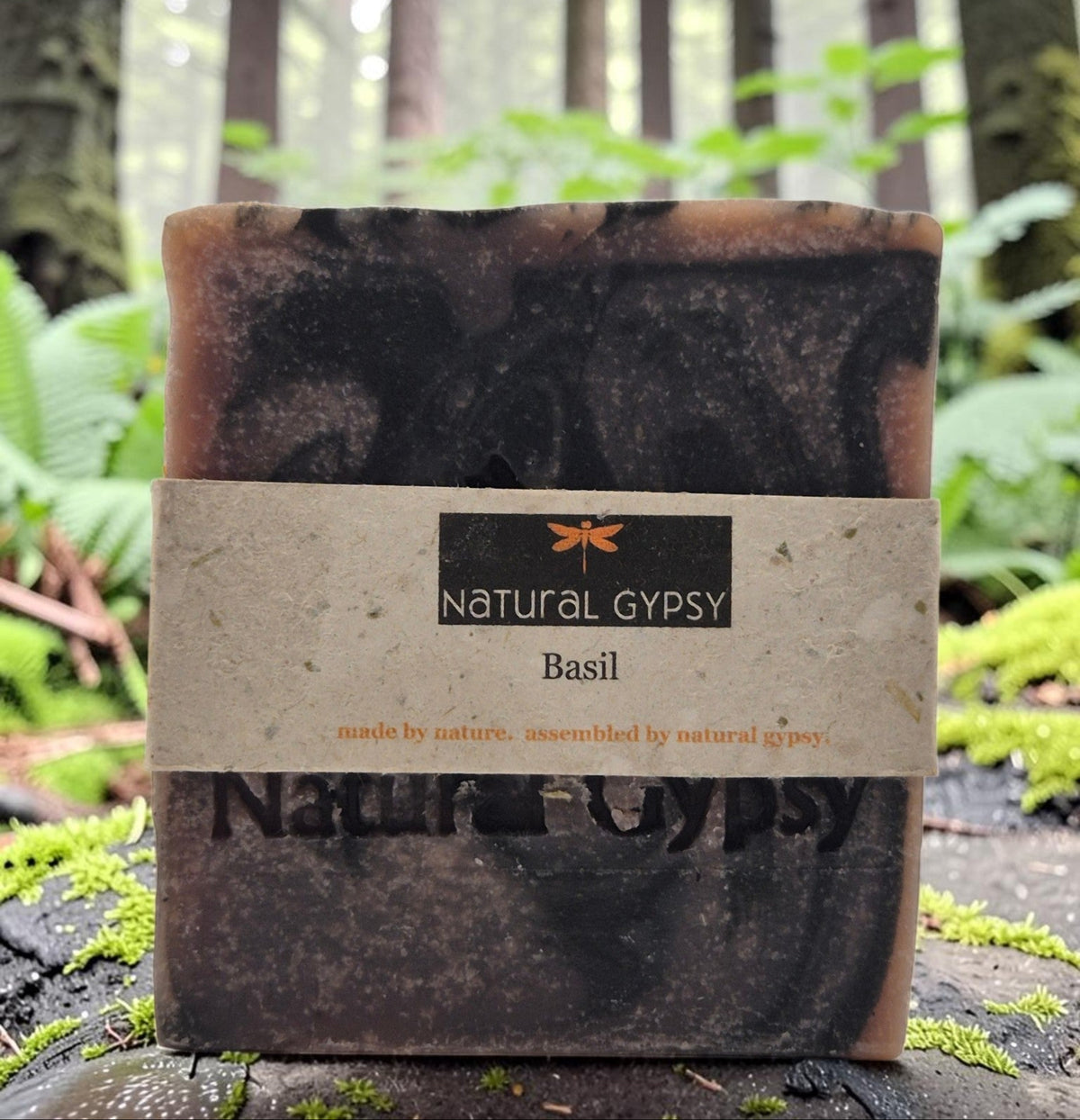 Natural Gypsy handcrafted basil artisan soap bar with a marbled brown texture, set against a misty forest background.
