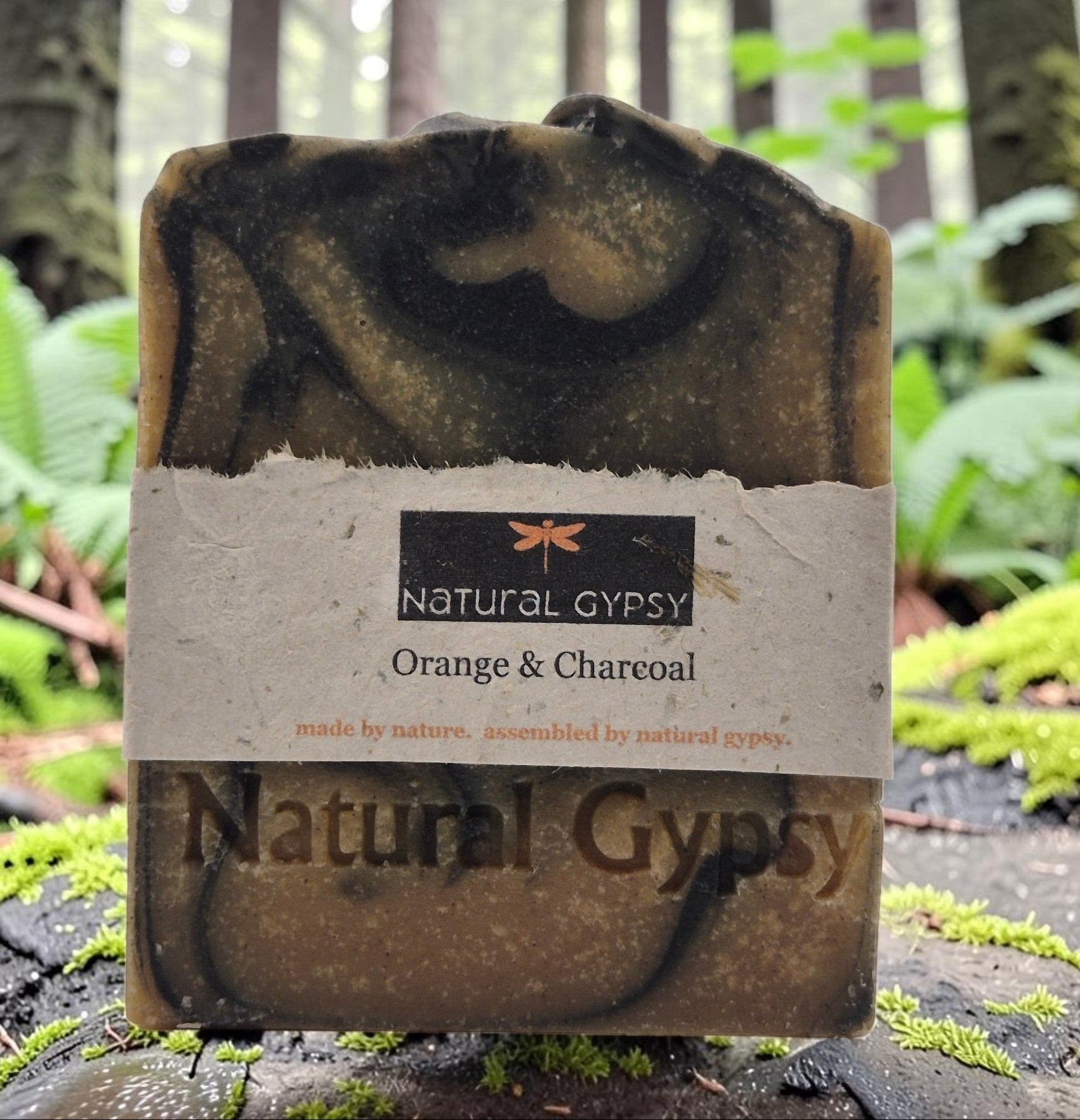 Natural Gypsy orange and charcoal artisan bar soap with a marbled texture, displayed on a mossy forest log.