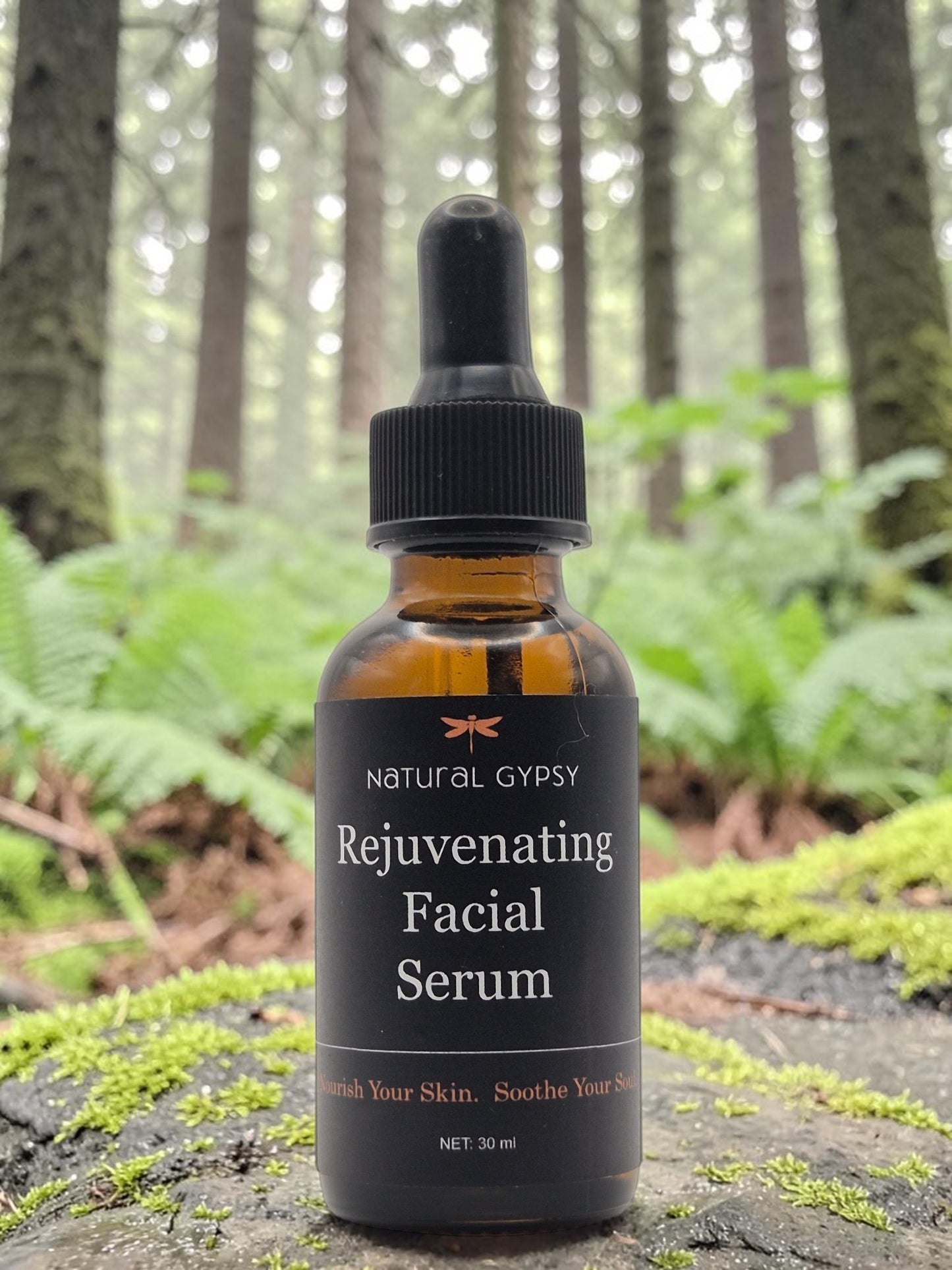 Natural Gypsy Rejuvenating Facial Serum in an amber glass dropper bottle, set on a mossy log in a forest.